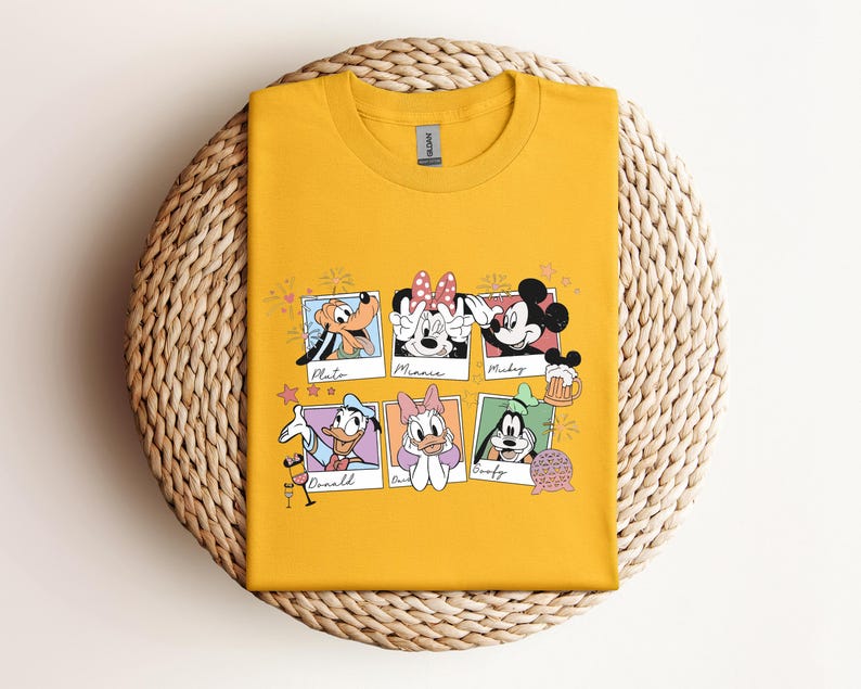May include: A mustard yellow crew neck t-shirt featuring a graphic print of six Polaroid-style frames. Each frame contains a Disney character illustration with their name written below: Pluto, Minnie, Mickey, Donald, Daisy, and Goofy.