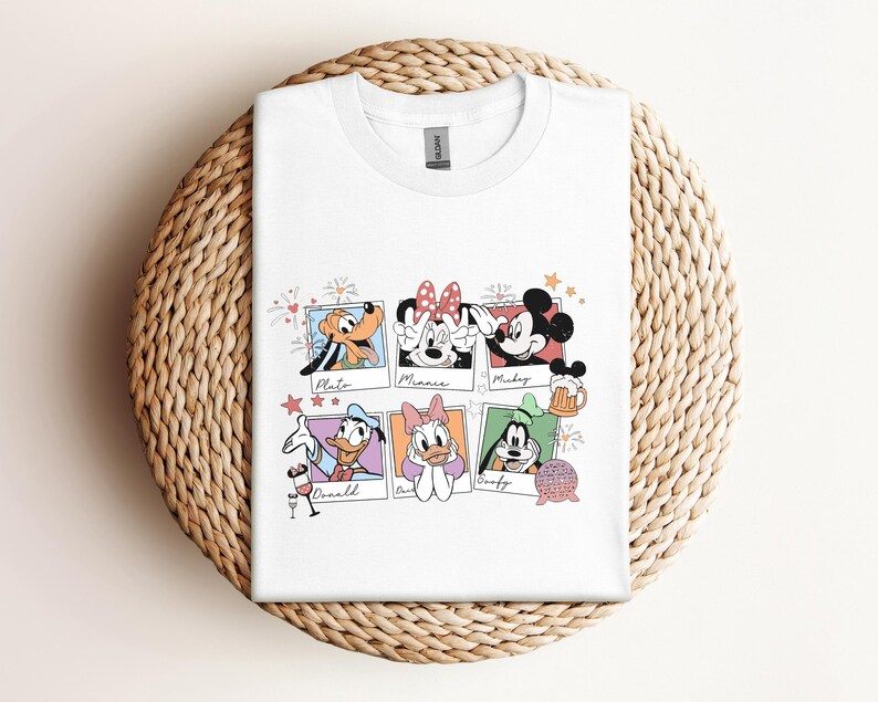 May include: A white crew neck t-shirt featuring a graphic print of six colorful polaroid-style frames. Each frame contains a cartoon character: Pluto, Minnie, Mickey, Donald, Daisy, and Goofy, with their names written in cursive script below.