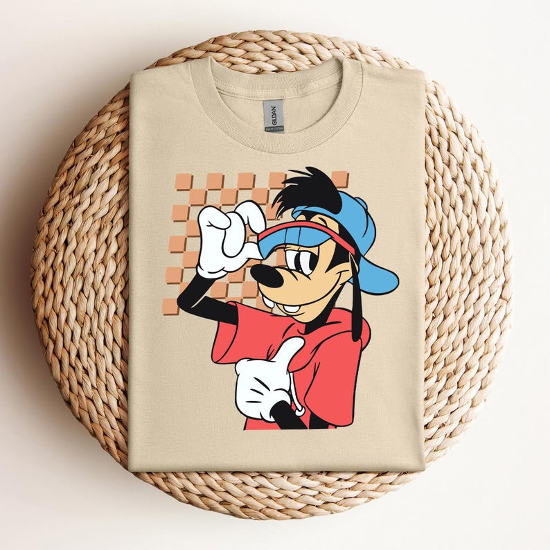 May include: A tan t-shirt with a cartoon image of Goofy wearing sunglasses, a red shirt, and a blue hat. The background is a checkered pattern.