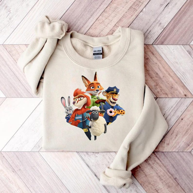 Op de afbeelding: Een cr&egrave;mekleurige sweatshirt met een kleurrijke afbeelding van personages uit de animatiefilm Zootopia. De afbeelding bevat een vos, een konijn, een schaap, een cheetah en een roodharig personage. De sweatshirt is gemaakt van een zacht materiaal.
