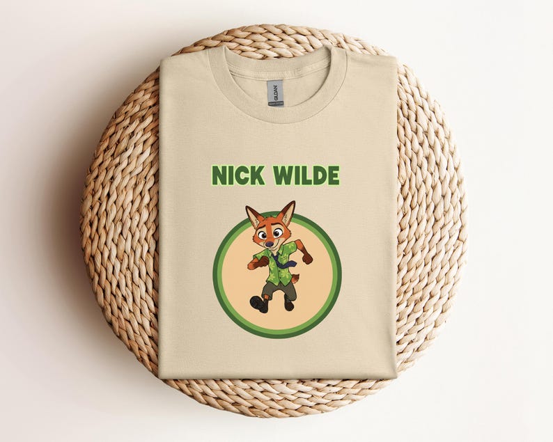 May include: Beige t-shirt featuring the name "NICK WILDE" in green block letters above a cartoon fox character inside a green and yellow circle. The fox is wearing a green shirt and tie.