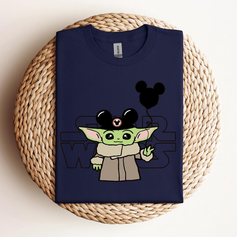 Puede incluir: Una camiseta azul marino con un personaje verde que lleva un sombrero de Mickey Mouse y sostiene un globo de Mickey Mouse. El texto "Star Wars" est&aacute; impreso en la camiseta.