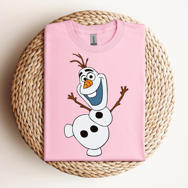 Pode incluir: Camiseta rosa com uma imagem de desenho animado de Olaf do filme Frozen. Olaf &eacute; um boneco de neve com um nariz de cenoura, olhos pretos e um grande sorriso. Ele usa um chap&eacute;u de galho de &aacute;rvore marrom e tem bra&ccedil;os de galho de &aacute;rvore marrom.