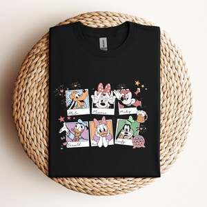May include: A black crew neck t-shirt featuring a graphic print of six polaroid-style frames. Each frame contains a Disney character: Pluto, Minnie Mouse, Mickey Mouse, Donald Duck, Daisy Duck, and Goofy, with their names written below each image.
