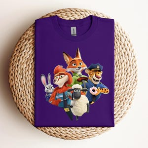 May include: A purple t-shirt featuring a colorful graphic of characters from the animated movie Zootopia. The design includes a fox, a rabbit, a sheep, a cheetah, and other characters. The shirt is folded and placed on a woven surface.