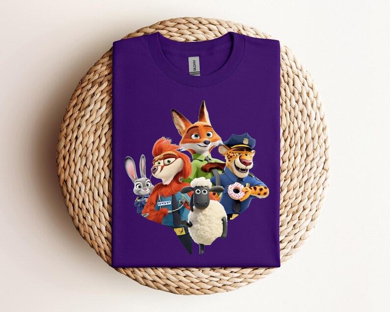 May include: A purple t-shirt featuring a colorful graphic of characters from the animated movie Zootopia. The design includes a fox, a rabbit, a sheep, a cheetah, and other characters. The shirt is folded and placed on a woven surface.