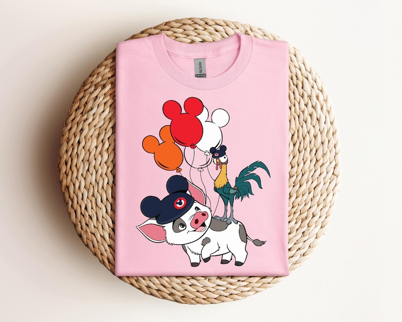 Op de afbeelding: Zachtroze T-shirt met een cartoonillustratie van een varken met een Mickey Mouse-hoed, een haan en rode, witte en oranje ballonnen. Het shirt is gemaakt van een zacht materiaal en is geschikt voor vrijetijdskleding.