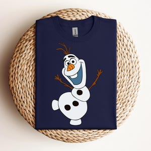 Pode incluir: Uma camiseta azul marinho com uma imagem de desenho animado de Olaf, o boneco de neve do filme Frozen, sorrindo e com os bra&ccedil;os estendidos.