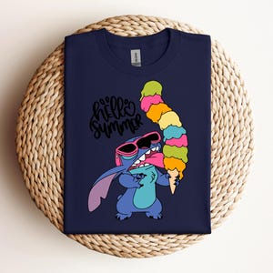 May include: Navy blue t-shirt featuring a cartoon character holding a large, colorful ice cream cone. The character wears sunglasses and the shirt has the text "hello summer" in a cursive font.