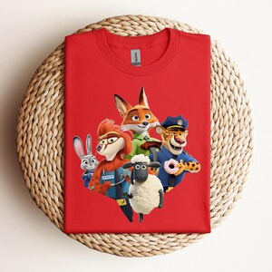 May include: A red t-shirt featuring a colorful graphic of characters from the animated movie Zootopia. The design includes a fox, a bunny, a sheep, a cheetah, and a red-haired character. The shirt is made of a soft material.