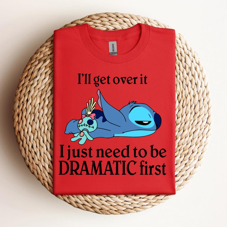 Puede incluir: Camiseta roja con un personaje azul Stitch de Lilo & Stitch. Stitch est&aacute; acostado con una peque&ntilde;a mu&ntilde;eca. El texto en la camiseta dice "I'll get over it I just need to be DRAMATIC first."
