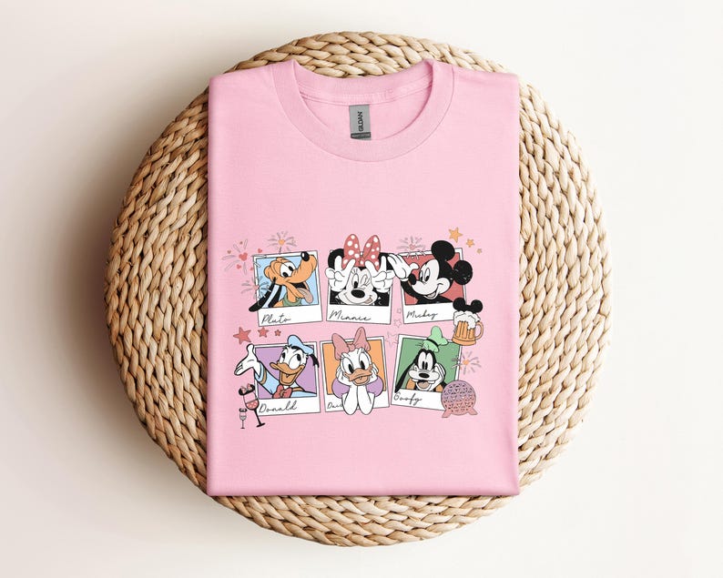 May include: A light pink short-sleeved t-shirt featuring a graphic print of six individual polaroid-style frames. Each frame contains a different Disney character: Pluto, Minnie Mouse, Mickey Mouse, Donald Duck, Daisy Duck, and Goofy.