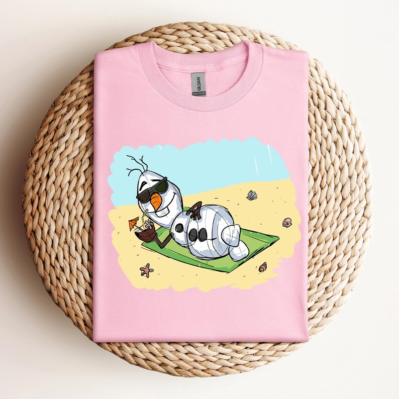 Op de afbeelding: Roze T-shirt met een cartoon afbeelding van Olaf uit Frozen, die een zonnebril draagt en ontspant op een strand met een kokosnootdrankje. De tekst "Let it Go" staat op het T-shirt gedrukt.