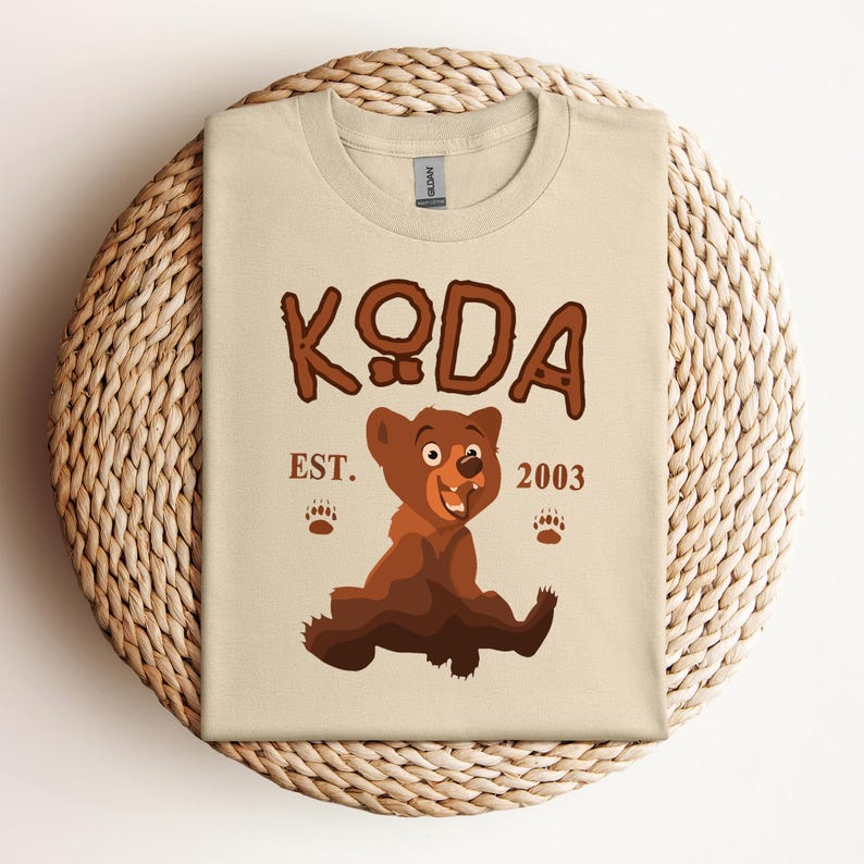May include: A beige t-shirt with a cartoon brown bear and the text "KODA EST. 2003".