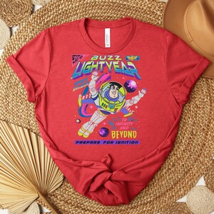 Puede incluir: Camiseta roja con un gr&aacute;fico de Buzz Lightyear en un traje espacial, con las palabras "Buzz Lightyear" y "To Infinity and Beyond". El dise&ntilde;o incluye planetas y estrellas, con la frase "Prepare for Ignition".