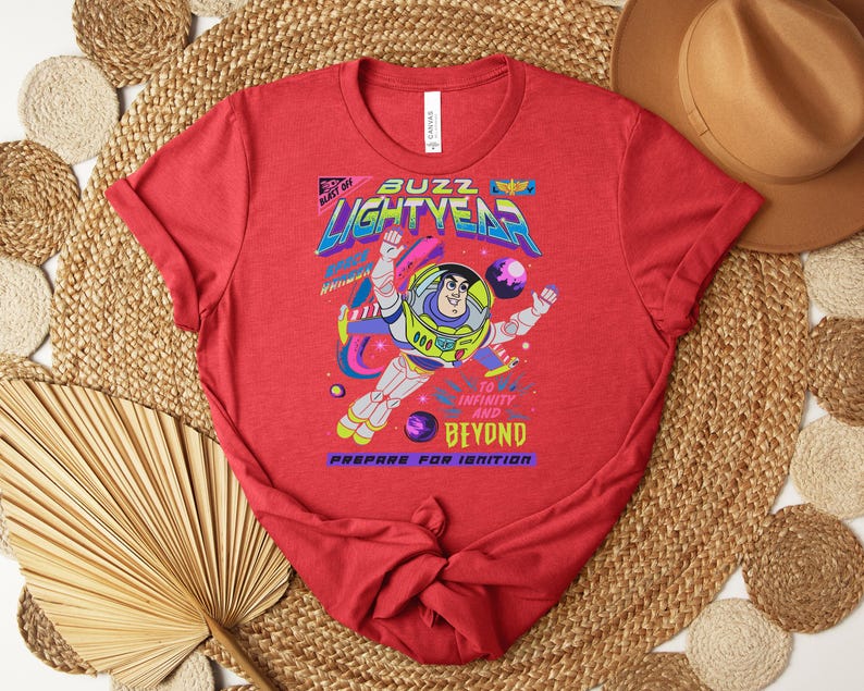 Puede incluir: Camiseta roja con un gr&aacute;fico de Buzz Lightyear en un traje espacial, con las palabras "Buzz Lightyear" y "To Infinity and Beyond". El dise&ntilde;o incluye planetas y estrellas, con la frase "Prepare for Ignition".