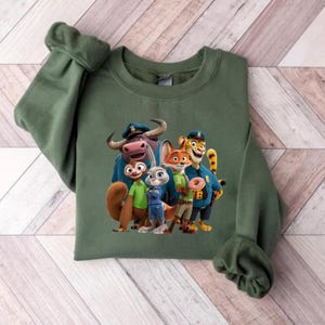 Puede incluir: Una sudadera verde con un gr&aacute;fico colorido de personajes de la pel&iacute;cula animada Zootopia. El dise&ntilde;o incluye un grupo de personajes animales con uniformes de polic&iacute;a y ropa casual. La sudadera est&aacute; hecha de un material suave.