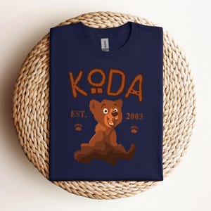 May include: A navy blue t-shirt with a cartoon bear and the text "KODA EST. 2003".