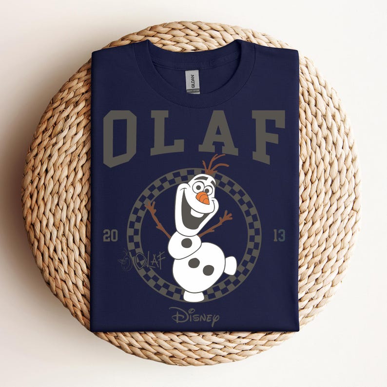 Może przedstawiać: Koszulka w kolorze granatowym z grafiką Olafa z Krainy Lodu. Grafika przedstawia Olafa w kwadratowym k&oacute;łku z napisem "Olaf" nad nim i "Disney" pod nim.