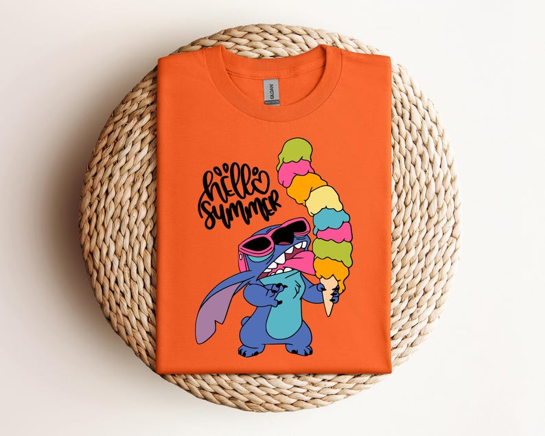 May include: Orange t-shirt featuring a cartoon character wearing sunglasses and holding a large ice cream cone. The text "hello summer" is written in black script. The shirt is folded on a woven, circular surface.