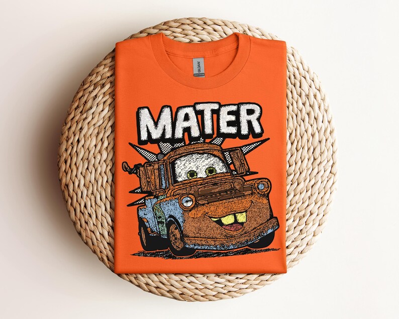 May include: Orange t-shirt featuring a graphic of Mater from the movie Cars. The word "MATER" is printed above the character in white block letters. The cartoon image of Mater is in shades of brown, blue, and green.