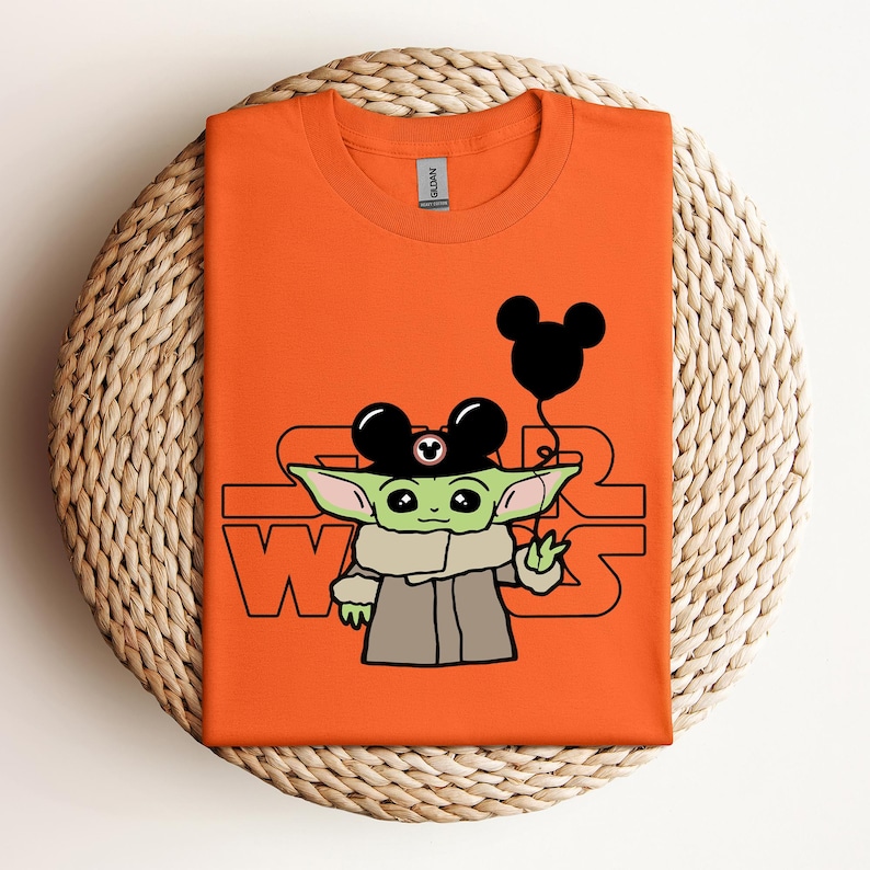Puede incluir: Camiseta naranja con un personaje alien&iacute;gena verde que lleva un sombrero de Mickey Mouse y sostiene un globo de Mickey Mouse. El texto "Star Wars" est&aacute; impreso en la camiseta.