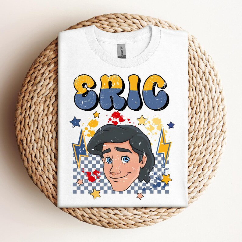 May include: White t-shirt featuring the name "ERIC" in yellow and blue retro font. Below the name is a cartoon illustration of a man's face with blue eyes and black hair. The design includes stars, lightning bolts, and a checkered pattern.