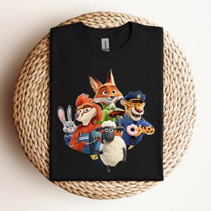 May include: Black t-shirt featuring a colorful graphic of characters from the animated movie Zootopia. The design includes a fox, a rabbit, a sheep, a cheetah, and other characters. The shirt is displayed on a woven, circular surface.