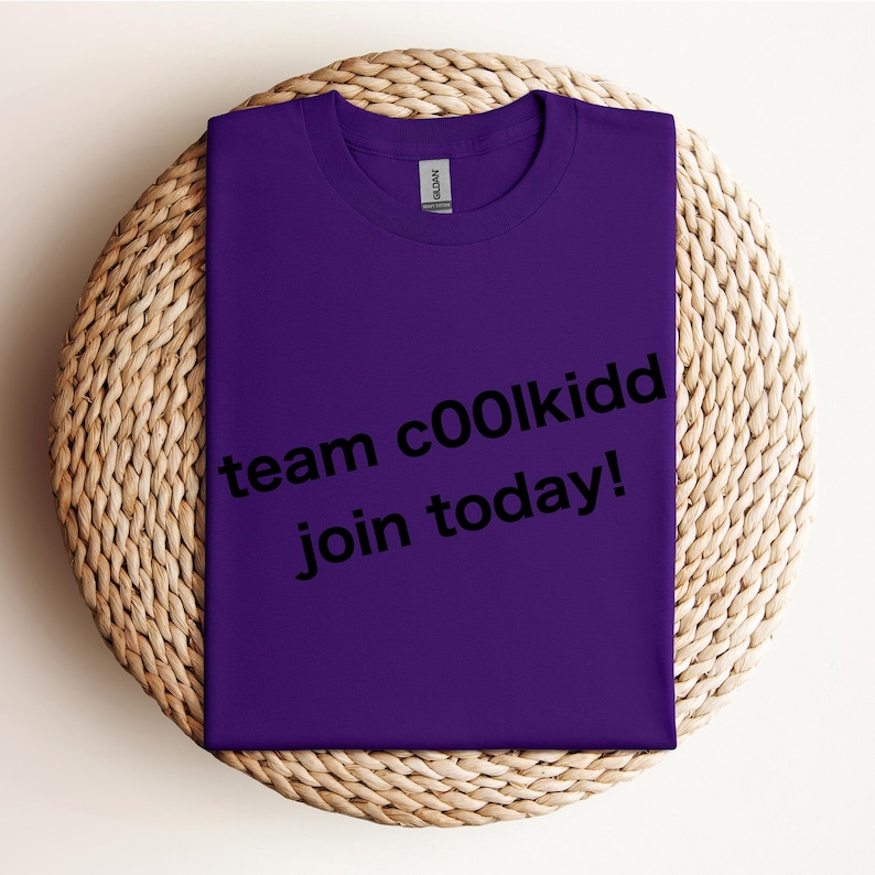 May include: A folded purple t-shirt with the text "team c00lkidd join today!" in black. The shirt is resting on a round, woven wicker placemat.