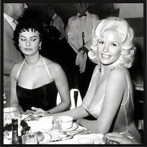 Peut inclure: Photographie encadrée en noir et blanc de deux femmes assises à une table. L'une porte une robe noire et un collier, l'autre une robe claire et des boucles d'oreilles. Des hommes en costume sont en arrière-plan.