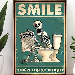 May include: A framed poster with a vintage aesthetic. The poster features a skeleton sitting on a toilet, reading a newspaper. The text "SMILE" is at the top, and "YOU'RE LOSING WEIGHT" is at the bottom, all in a distressed font.