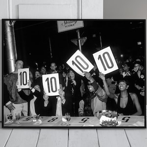 Può includere: Stampa incorniciata in bianco e nero di un evento vivace. Le persone alzano cartelli con il numero 10. Un cartello per "Sterling Vodka" è visibile. La scena include un tavolo con bicchieri e una ciotola.