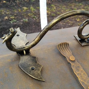 May include: A gold-colored metal dragon-shaped door handle with a curled tail. The handle is attached to a metal plate with two screws. The handle is mounted on a brown metal surface.