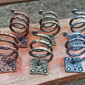 May include: Six metal spiral hooks with a hammered finish. The hooks are mounted on square bases and are available in copper, silver, and black.
