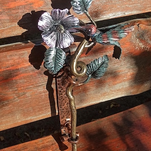Könnte beinhalten: Handgefertigter Türgriff aus Metall mit einem Design aus Kolibri, Blume und Blättern. Der Griff besteht aus Kupfer und Bronze mit grünen, roten und silbernen Akzenten. Der Griff ist auf einer Kupferplatte montiert. Für Türen oder Schränke.