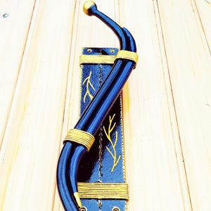 Peut inclure: Un crochet mural décoratif avec un design incurvé en métal bleu foncé et des accents dorés. Le crochet est monté sur une base rectangulaire bleue avec des détails dorés en forme de feuilles et une bordure dorée.