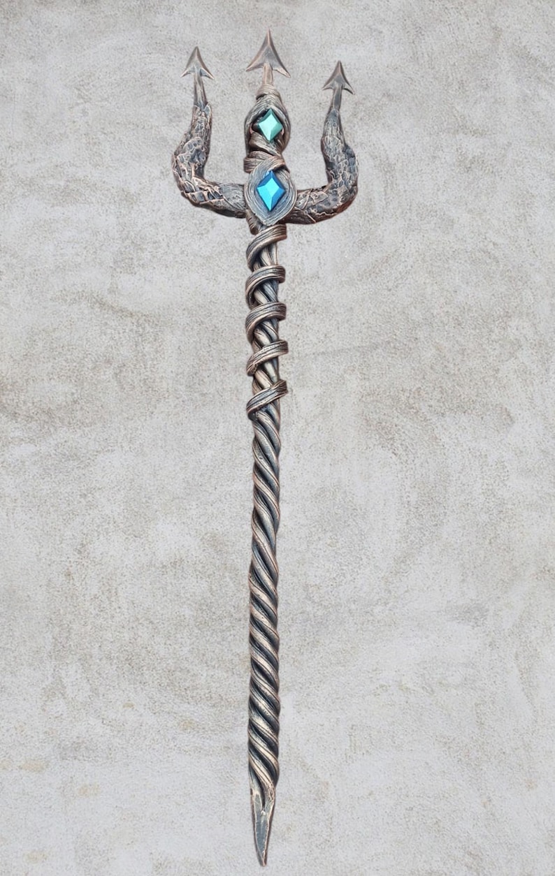 May include: A silver trident with a twisted handle and three prongs. The prongs are decorated with a snake-like design. The handle is adorned with two blue and green gemstones.