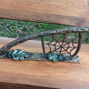 May include: A metal handrail with a branch design and a spiderweb motif. The handrail is decorated with green leaves and has a brown finish.