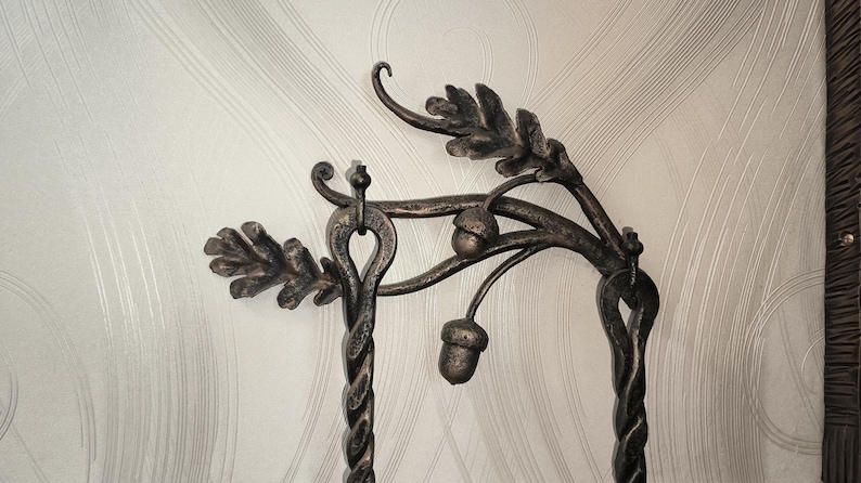 Peut inclure: Support d&eacute;coratif en m&eacute;tal fonc&eacute; orn&eacute; de feuilles de ch&ecirc;ne et de glands. Il pr&eacute;sente une base en colonne torsad&eacute;e et un sommet incurv&eacute; avec des d&eacute;tails de feuilles et de glands. Le m&eacute;tal a un aspect vieilli et rustique.