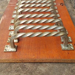 Peut inclure: Ensemble de poignées métalliques de style ancien avec un design torsadé, montées sur une planche de bois brun rougeâtre. Les poignées sont disposées en rangée, mettant en valeur leur aspect décoratif.
