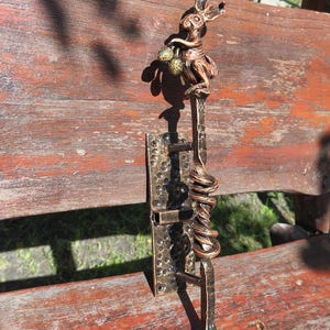 Könnte beinhalten: Ein bronzefarbener Türgriff aus Metall mit einer skulptierten Hasenfigur an der Oberseite, die zwei kleine, texturierte Kugeln hält. Der Griff hat einen gedrehten Mittelteil und ist auf einer rechteckigen Platte mit gehämmertem Finish montiert.