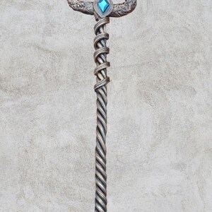 May include: A silver trident with a twisted handle and two blue gemstones. The trident is on a gray background.