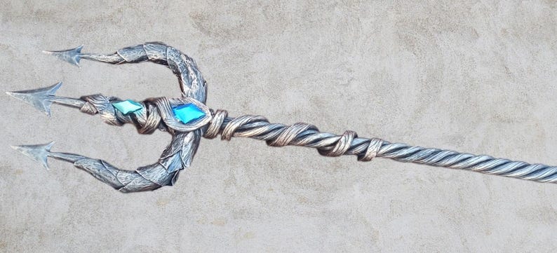 May include: A silver trident with a twisted handle and blue and green gemstones. The trident is a fantasy prop.
