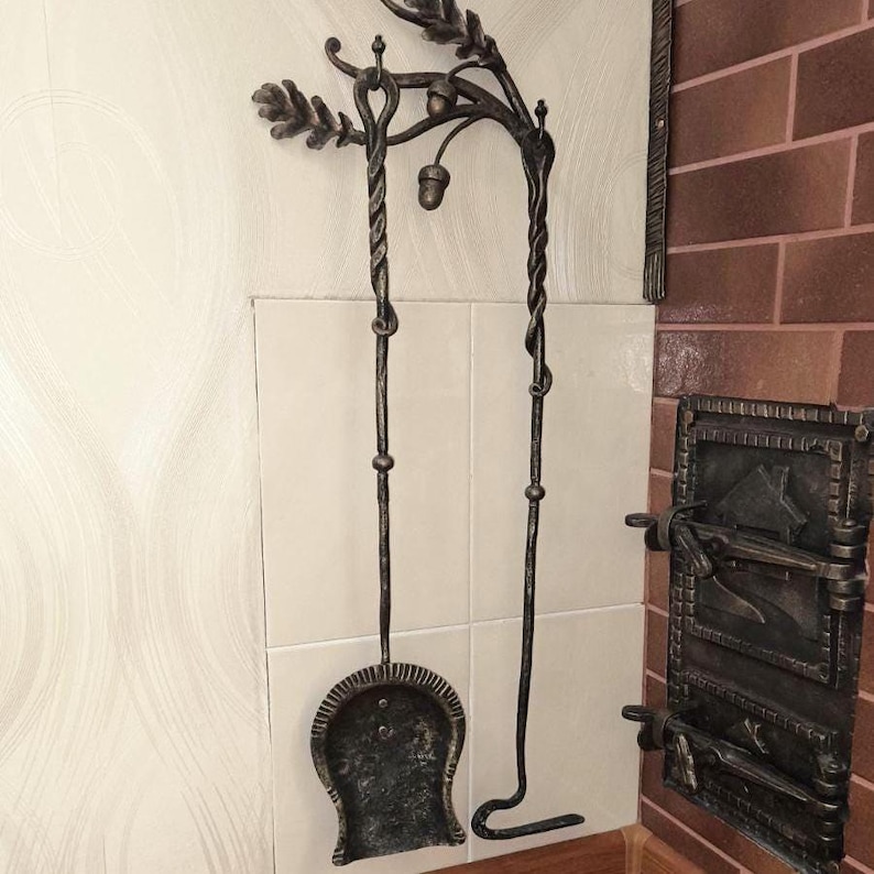 Peut inclure: Ensemble d'outils de chemin&eacute;e forg&eacute;s &agrave; la main, avec un motif de feuilles de ch&ecirc;ne et de glands. L'ensemble comprend une pelle et un tisonnier, avec des manches en m&eacute;tal torsad&eacute;. Les outils sont fix&eacute;s au mur avec un support d&eacute;coratif.