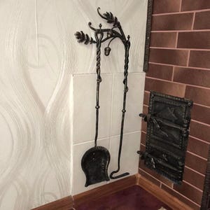 Peut inclure: Ensemble d'outils de chemin&eacute;e en fer forg&eacute; noir, comprenant une pelle, un tisonnier et un support. L'ensemble pr&eacute;sente des d&eacute;tails de feuilles et de glands. Les outils sont mont&eacute;s sur un mur carrel&eacute; blanc &agrave; c&ocirc;t&eacute; d'une chemin&eacute;e en briques.
