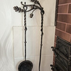 Peut inclure: Ensemble d'outils de chemin&eacute;e forg&eacute;s &agrave; la main. L'ensemble comprend une pelle et un tisonnier, tous deux avec des poign&eacute;es torsad&eacute;es et des accents d&eacute;coratifs de feuilles et de glands. Les outils sont en m&eacute;tal fonc&eacute; et mont&eacute;s sur un mur.