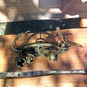 May include: A metal wall decor featuring a dragonfly perched on a branch with three stylized flowers. The dragonfly and flowers are painted in gold and black.