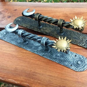 May include: Two black metal door handles with a twisted design. One handle features a silver crescent moon and the other features a gold sun.