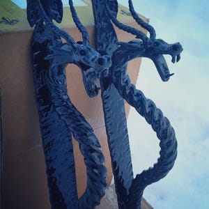 May include: Two black metal dragon door handles with a twisted rope design. The handles are in a vertical position and are partially obscured by a cardboard box.