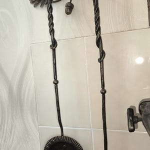 Peut inclure: Un ensemble d'outils de chemin&eacute;e en fer forg&eacute; avec un motif de feuilles de ch&ecirc;ne et de glands. L'ensemble comprend une pelle et un tisonnier avec des poign&eacute;es torsad&eacute;es et une finition sombre et vieillie. Les outils sont fix&eacute;s au mur.